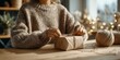 © MNStudio - Young woman in a chunky knitted sweater wraps a gift with kraft paper and string by a window. Warm, natural winter ambiance.