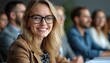 © miss irine - Smiling woman wearing glasses at meeting. Businesswoman attends conference. Blond hair female portrait in pro environment. People listen, discuss. Corporate team working indoors during event in