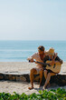© Mirrorstudio - Caucasian couple relaxing on beach playing guitar on a sunny day