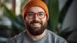 © Bella - Warm portrait of a cheerful bearded man wearing an orange beanie and bright eyewear, captured in soft natural light with a cozy indoor atmosphere that highlights his friendly expression and relaxed mo