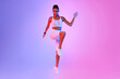 © Prostock-studio - A fitness enthusiast executes a standing crunch by raising her knee in a neon pink and blue studio. She looks confidently at the camera while working on her cardio routine.
