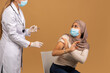 © Prostock-studio - Young arab lady in face mask scared to make coronavirus vaccine injection, making STOP gesture and looking at doctor. Muslim woman opposing immunization against covid-19