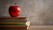 © ai - A red apple rests on a stack of colorful books placed on a wooden surface against a concrete wall background.