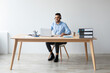 © Prostock-studio - Smiling Arab man sits at a desk in a modern office, using a laptop and headset for online client consultations. He appears focused and happy in his work environment.