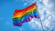 © Wattana - A rainbow flag waving in the wind against a blue sky with white clouds.