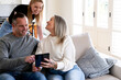 © Austockphoto - Couple with their teenage daughter engaged on a digital phone while seated on the couch