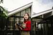 © Worawi - A woman wearing an apron holds a tablet while working outdoors in front of a modern building.