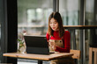 © Worawi - A woman sitting in a cafe working on a tablet while checking her smartphone, with coffee and a small plant on the table.
