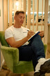 © Cristian Blázquez - Man writing in notebook sitting in armchair at home
