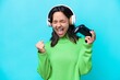 © luismolinero - Young hispanic woman playing with a video game controller isolated on blue background celebrating a victory