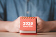 © Dilok - Desk calendar showing 2026 start in front of businessman which symbolizing new year beginning business planning fresh goals and motivation for future success and positive change concept