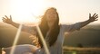 © Youlie - Happy young woman with long hair smiling freely with her arms outstretched in a sunny field at sunset, embracing the warm light and feeling pure joy