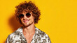 © Oleksandr - Smiling man with curly hair and sunglasses against yellow background. He's wearing a floral shirt and looking stylish for summer vacation. Great for travel ads!