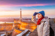 © EdNurg - Young woman smiling, sightseeing in Belgrade, wearing winter clothes, enjoying beautiful sunset sky over the old city