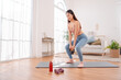© Kiattisak - Fitness training at home with kettlebell workout. Asian woman on yoga mat, building strength and toning muscles in cozy living room setting.
