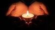 © Shipna - Cupped hands gently hold a lit candle, casting a warm glow in the darkness, symbolizing hope and remembrance