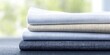 © Konstiantyn Zapylaie - Stack of folded linen fabrics in neutral colors on blue surface