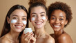 © Vadym - Three smiling diverse women apply white face cream in studio. Skincare routine for healthy glowing skin. Beauty products for pampering and self care.