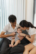 © kamiphotos - A young family shares tender moments with their baby in a cozy home. The father kisses the baby tiny hand and foot while the mother holds the infant lovingly, symbolizing warmth and care.
