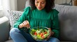 © Zohaib - Fat woman eating healthy food.  shot of chubby plump overweight girl sitting on couch holding glass bowl of fresh vegetable salad. Healthy diet and weight loss concept