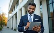 © Anthony - Focused successful mature Indian or Latin entrepreneur businessman holding digital pc tablet standing outdoor at business office building. Hispanic smiling man in suit working using touchpad computer