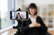 © Sofiia Shunkina - Caucasian woman in early 30s in business suit recording video content in office setting. Concept includes leadership, modern technology, and communication. Scene portrays professionalism.