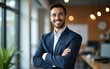 © Samuel - Smiling young businessman standing with his arms crossed at work. High quality