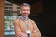 © Cristina Garcia - Mature man smiling with crossed arms wearing a lanyard and an id badge near an office building