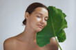 © Buyanskyy Production - Serene Woman with Eyes Closed Holding Large Green Leaf in Skincare Concept