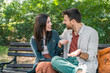 © Srdjan - Young couple cuddling on a park bench, smiling and leaning in for a kiss, sharing an affectionate embrace in sunny green nature casual outfits, warm connection, romantic date outdoors