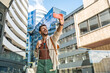 © Srdjan - Young traveler laughing while taking a selfie in a modern business district cheerful millennial man with backpack capturing urban architecture and city vibes on smartphone during a sunny day