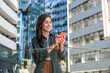 © Srdjan - Smiling young woman on phone call in modern business district cheerful traveler with backpack, chatting on smartphone amid sleek urban architecture and reflective office towers on a sunny day