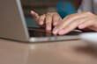 © iqbal - A close-up of a young Muslim woman’s hand on a laptop working remotely from a modern cafe. The batik sleeve reflects a blend of culture and modern professionalism.