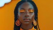© Kadal - A close-up portrait of a woman with vibrant makeup and dreadlocks, eyes closed against orange background