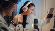 © tirachard - Close-up Young happy Asia couple wear headphone sit on desk online live streaming football live score watch soccer sport game on laptop use microphone talk with follower small studio in home at night.