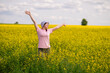 © kazakova0684 - Woman in bucket hat raising arms up, enjoying a warm summer day in a blooming yellow rapeseed field