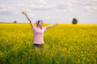© kazakova0684 - Woman in bucket hat raising arms up, enjoying a warm summer day in a blooming yellow rapeseed field