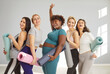© Studio Romantic - Happy group of young sporty girls, afro american woman and caucasian fit people with yoga mats standing, female companions in gym after fitness, instructor and club team after practicing sport lesson
