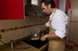 © Taras Grebinets - Man Cooking In Kitchen With Apron At Stove, Preparing Food In Wok, Home Cooking Scene