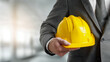 © Yurij - Businessman or engineer in formal suit holding a yellow construction helmet symbolizing safety and professionalism in construction industry environment