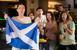 © JackF - Cheerful football fans waving the flag of Scotland while drinking beer and watching tournament in sport bar