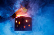 © st.kolesnikov - Hands lifting glowing mystery gift box with smoke and stars on blue background