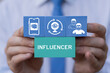 © wladimir1804 - Business person holding blocks with icons sees the word INFLUENCER. Concept of influencer, follower, social media, promotion, passion, celebrity, influence, content, community and marketing.