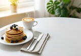 Morning indulgence: Fluffy pancakes with blueberries, maple syrup and a warm cup of latte art on a pristine white table