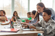 © Prostock-studio - In a bright classroom, a teacher assists a group of diverse school children as they engage with laptops. The students, including an African American boy, explore online learning together.