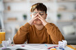© Prostock-studio - Overweight Japanese teenager is sitting at his desk doing a school project. He rubs his eyes in fatigue while surrounded by books and crumpled papers, seeking creative solutions.