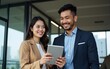 © Michael - Two happy professional business people team Asian woman and Latin man workers working using digital tablet tech discussing financial market data standing at corporate office meeting. High quality