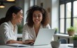 © Robert - Two professional women collaborating happily over laptop in modern office. High quality
