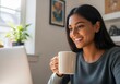 © ZHMPRO - Smiling young indian woman enjoying a cup of coffee while working on her laptop at home, looking at the screen with a happy expression