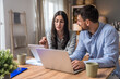 © Srdjan - Couple reviewing household budget at home woman with coffee and tablet, man focused on laptop; paperwork on table in cozy living room, finances, bills, savings, remote work.
